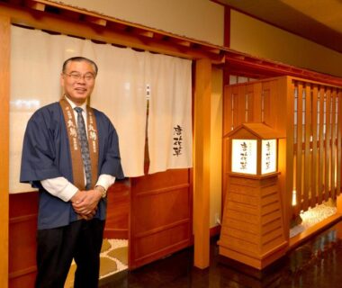 Smiling staff member by wooden noren and lantern at Marukoma Onsen Ryokan in Hokkaidō Japan