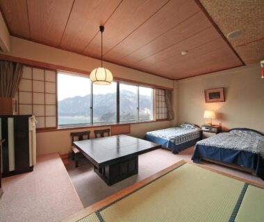 Tatami flooring, low table, twin beds and shoji window with distant mountain view at Sarugakyo Hotel, Gunma