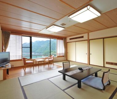 Spacious tatami room with low table, cushions and large window framing mountain view at Sarugakyo Hotel in Gunma
