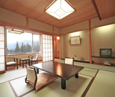 Tatami room with low wooden table, zaisu chairs, shoji screens and framed art at Sarugakyo Hotel, Gunma, Japan