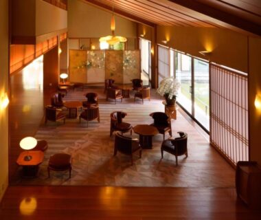 Warm-lit ryokan lounge with low chairs, round tables, shoji screens and wooden ceiling at Saryo Souen in Miyagi