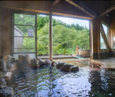 Indoor rock-lined onsen bath with large windows overlooking forest at Sasakura onsen Ryuunso, Niigata Chūbu