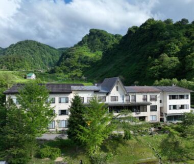 Three-story ryokan building nestled in green mountains by a river, Sasakura onsen Ryuunso, Niigata