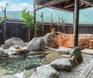 Stone-lined onsen with wooden deck and rock bath at Sasara, mountain backdrop in Chūbu Gifu