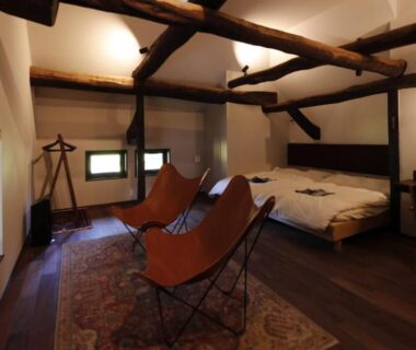 Interior with exposed wooden beams, twin beds and leather lounge chairs, Satoyama Jujo The House, Niigata, Chūbu Japan