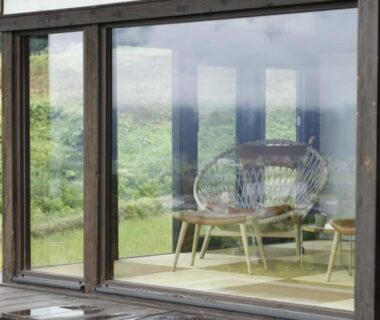 Tatami seating with woven chairs beside floor-to-ceiling windows overlooking green fields at Satoyama Jujo in Niigata