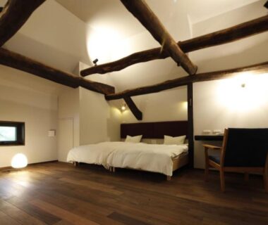 Low bed beneath exposed wooden beams with desk and warm lighting at Satoyama Jujo The House, Niigata