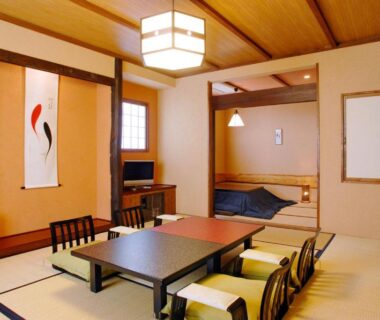 Spacious tatami room with low dining table, zabuton cushions, tokonoma alcove and futon area at Sawaemon Nagano