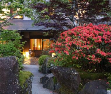 Mossy stone path through garden to Sawaemon entrance with blooming shrubs and warm lantern lighting