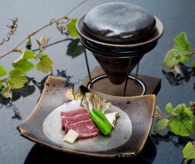 Raw beef slices with vegetables beside a small tabletop grill and vine decoration at Sawaemon in Nagano