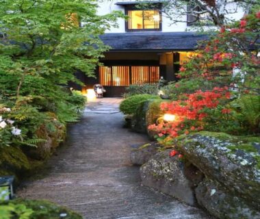 Stone garden path with mossy rocks and illuminated entrance at Sawaemon ryokan in Nagano, Chūbu