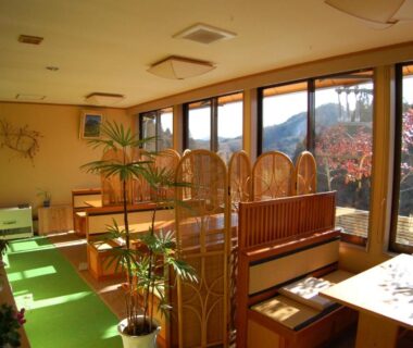 Bright wooden dining lounge with booths, low tables, plants and mountain view at Sawatari Onsen Miyataya Ryokan, Gunma
