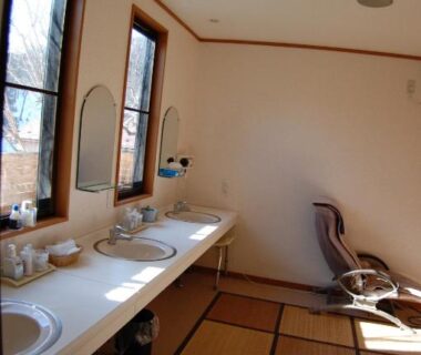 Shared wash area with double sinks, mirrors, tatami flooring and reclining chair at Sawatari Onsen Miyataya Ryokan, Gunma