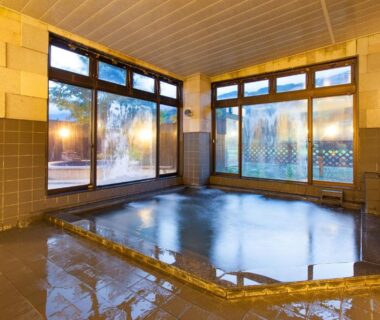 Tiled indoor onsen with wooden ceiling and large windows at Schole Hakuba, Nagano