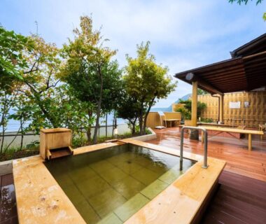 Outdoor wooden onsen bath on deck with sea beyond trees at Seaside Hotel Mimatsu Ooetei, Oita