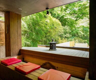 Open wooden veranda with red cushions and lantern overlooking lush green foliage at Seikansou in Kanagawa
