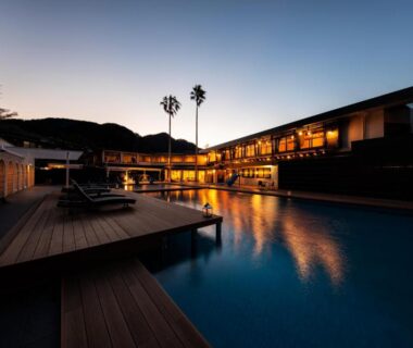 Evening outdoor pool with wooden deck, lit Seiryu-so building reflecting in water, palm trees and twilight sky