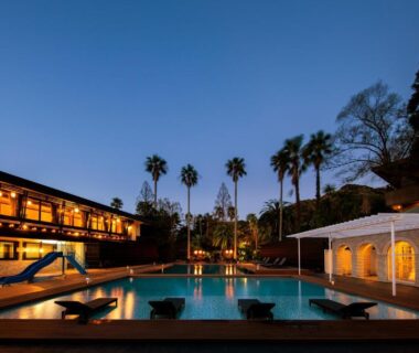 Outdoor illuminated swimming pool with slide and lit ryokan buildings at dusk with palm trees