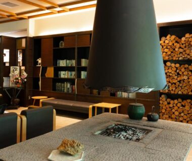 Warm lounge with sunken hearth, suspended hood, stacked firewood and seating at Seiryukaku, Iwate