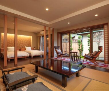Tatami room with low wooden table, lounge chairs and twin beds opening to garden at Sekitaitei Ishida Nagano