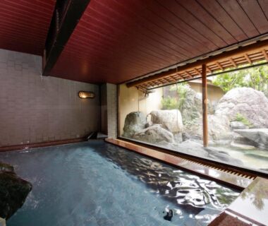 Indoor onsen bath facing a rock garden through large glass window at Sekitaitei Ishida Nagano