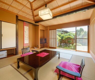 Traditional tatami room with low table, cushions and sliding doors opening to a small garden at Sekitaitei Ishida, Nagano