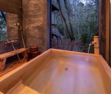 Wooden soaking tub with bench and shower beside large window overlooking forest at Sen-no-Mori, Kumamoto Kyūshū