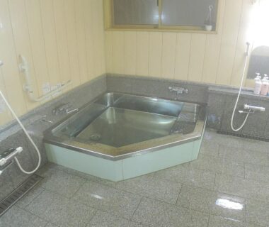 Tiled bathing area with corner hexagonal tub, wall-mounted hand showers and small window at Sendaiya Gifu