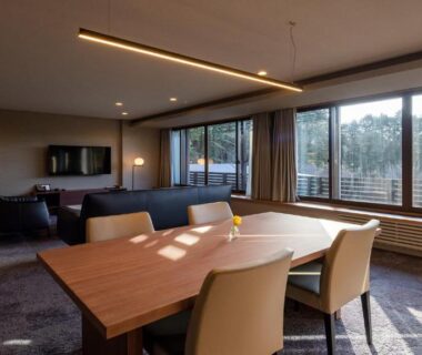 Dining area with table, sofa and large windows at Sengokubara COCON, Kanagawa, overlooking trees