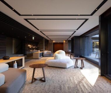 Spacious modern lounge with low seating, wooden accents and floor-to-ceiling windows overlooking a courtyard garden