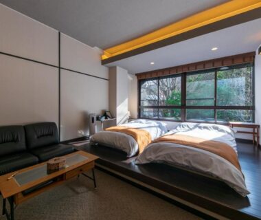 Twin beds on raised wooden platform with low table, sofa and large window overlooking a garden at Sengokuhara Hisanoha, Kanagawa