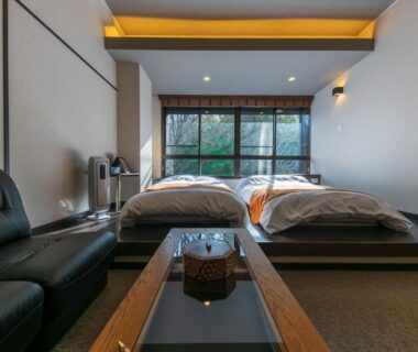 Twin beds on raised platform with low table and sofa, large window showing garden greenery at Sengokuhara Hisanoha Kanagawa