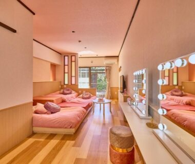 Bright room with wooden floor, pink bedding, dressing vanity and sliding glass doors to garden view