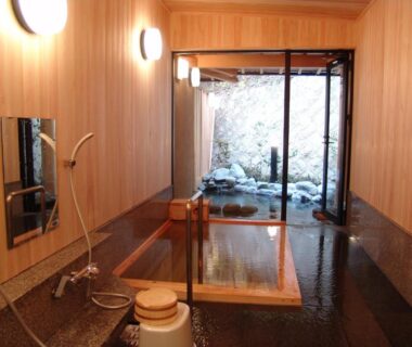 Indoor wooden bathing area with soaking tub, shower stool and stone garden view