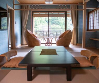 Tatami room with low table, floor cushions, shoji screens and balcony seating overlooking greenery at Senkei, Kanagawa