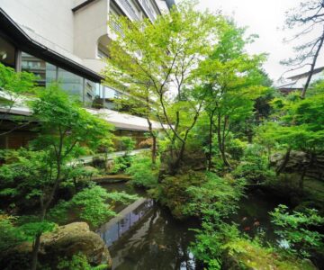 Lush moss garden with reflecting pond, stone accents and surrounding hotel wings at Senkeien Tsukioka Hotel Yamagata