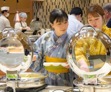 Two guests in yukata selecting dishes at a buffet counter inside Senkeien Tsukioka Hotel dining area in Yamagata