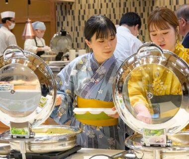 Two guests in yukata selecting dishes at a buffet counter inside Senkeien Tsukioka Hotel dining area in Yamagata
