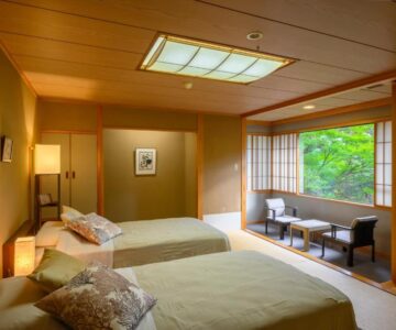 Tatami room with twin beds, shoji screens and seating by a garden-facing window at Senkeien Tsukioka Hotel, Yamagata