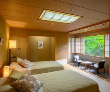 Tatami room with twin beds, shoji screens and seating by a garden-facing window at Senkeien Tsukioka Hotel, Yamagata