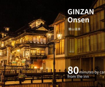 Illuminated wooden onsen buildings along a riverside at night near Senkeien Tsukioka Hotel Yamagata