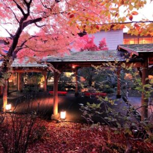Lit courtyard with red maple leaves, wooden walkway and traditional ryokan exterior at dusk in Gunma