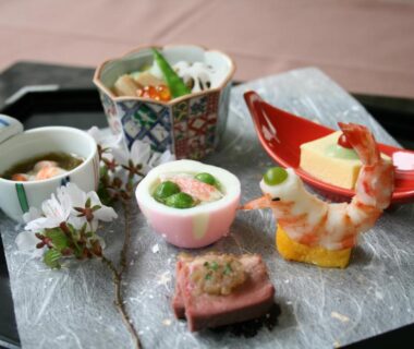 Delicate selection of small plated Japanese appetizers including shrimp and tofu served on lacquer tray