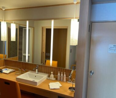Sink and wooden vanity with illuminated mirrors, toiletries and seating at Senoumi ryokan washroom in Shizuoka