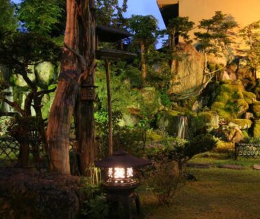 Evening-lit ryokan garden with stone lantern, trees and landscaped rocks at Senshoen in Hokkaido