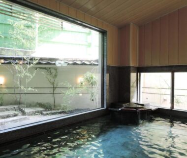 Indoor onsen bath with large window overlooking a small courtyard garden at Senso Yutagawa, Yamagata