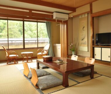 Tatami room with low table, zabuton cushions and window overlooking trees at Senso Yutagawa, Yamagata