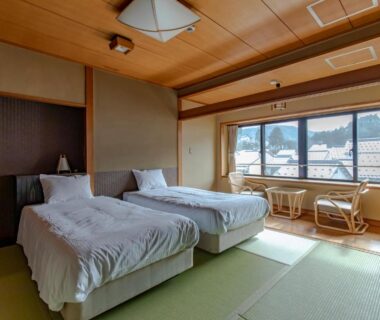 Tatami-floored room with twin beds, low table seating by window and town and mountain view in Hyōgo