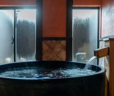 Round wooden soaking tub with steaming windows in intimate indoor onsen room at Sensui Hyōgo
