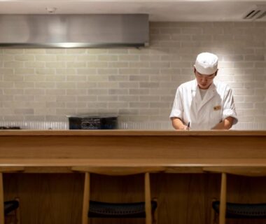 Chef preparing dishes behind a wooden counter with stools at Sensui ryokan in Hyōgo, Kansai